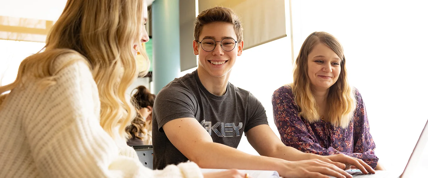 Groupe d'étudiants et étudiantes souriants devant un ordinateur portable